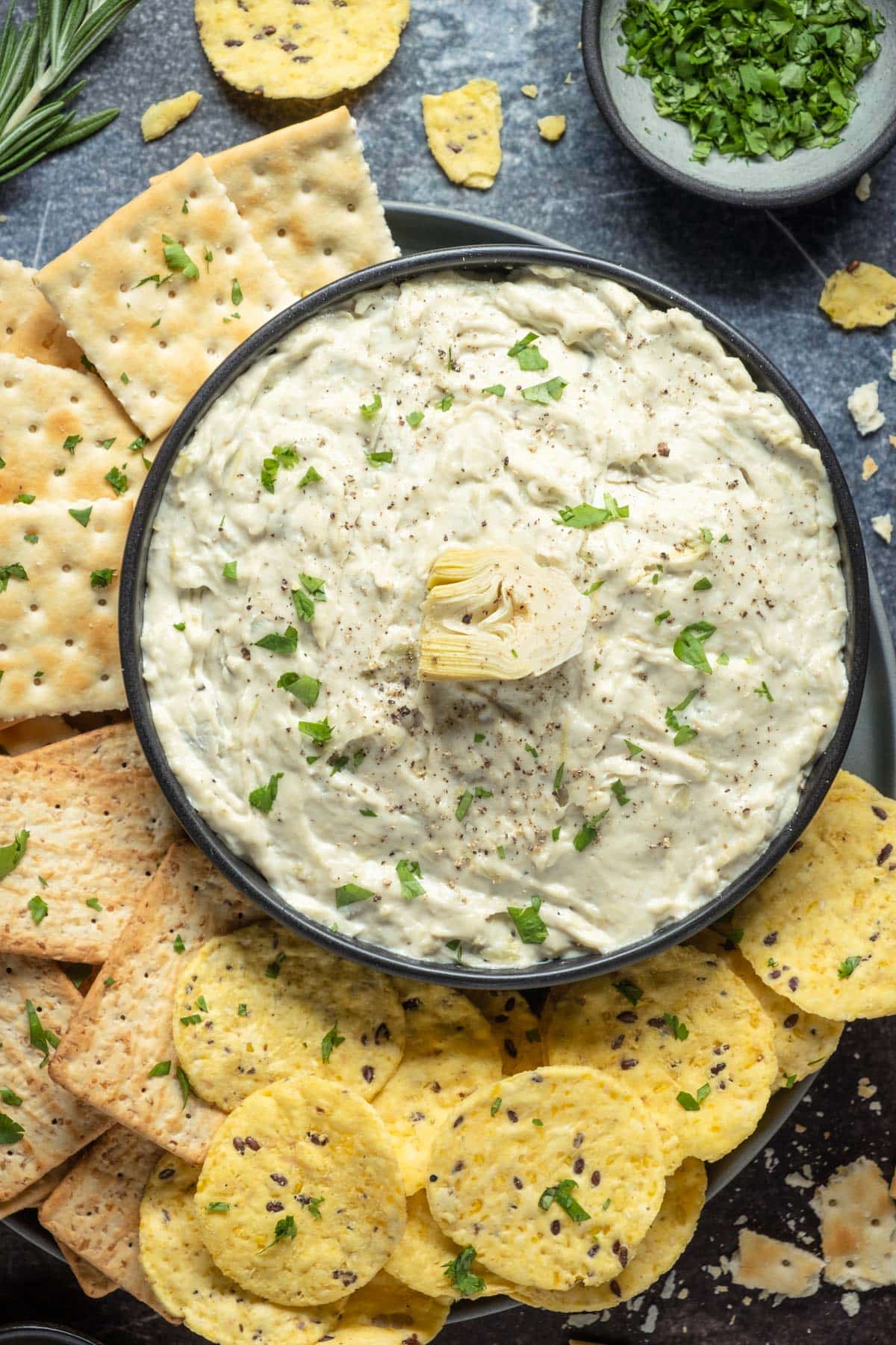 Vegan artichoke dip in a black bowl surrounded by crackers. 